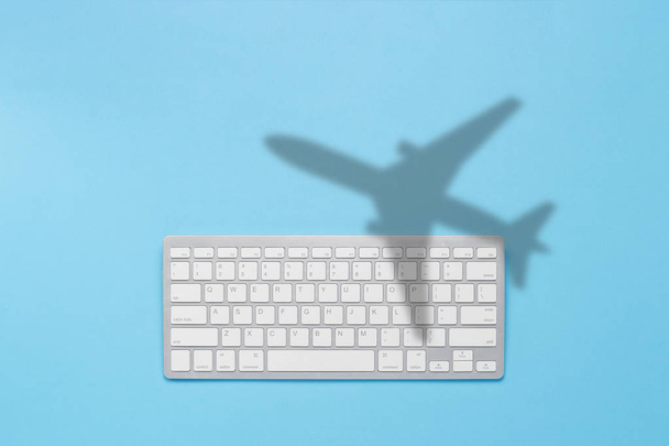 Клавиатура и тень летающего самолета на синем фоне. Концепция покупки билетов в интернете, бронирование билетов. Плоский, вид сверху
 - Фото, изображение