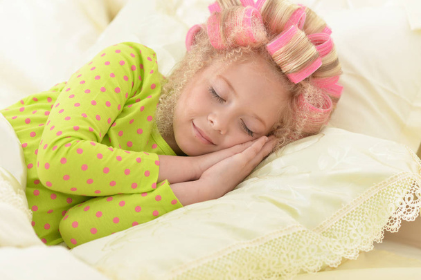 Lovely little girl with pink curlers sleeping in bed at home - Foto, imagen