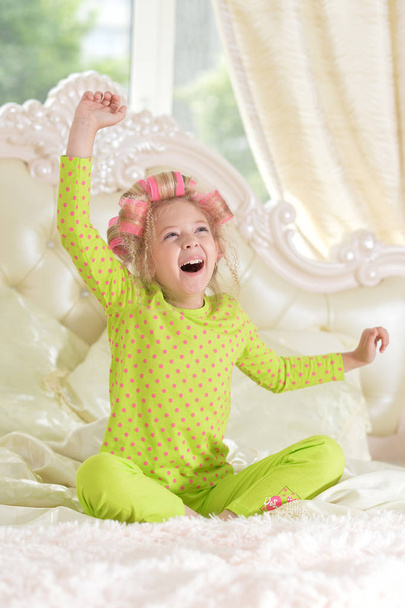Lovely little girl with pink curlers having fun on bed at home - Valokuva, kuva