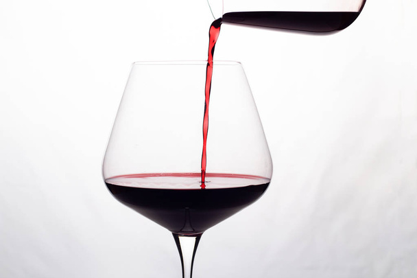 punaviini kaadetaan viinilasiin valkoisella pohjalla
 - Valokuva, kuva