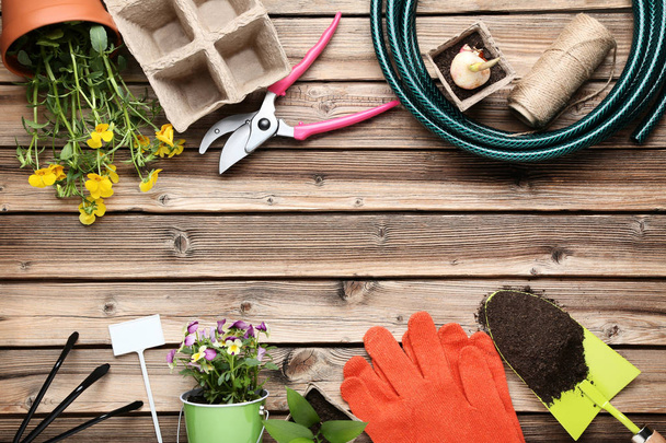 Diferentes herramientas de jardín con flores en mesa de madera
 - Foto, imagen