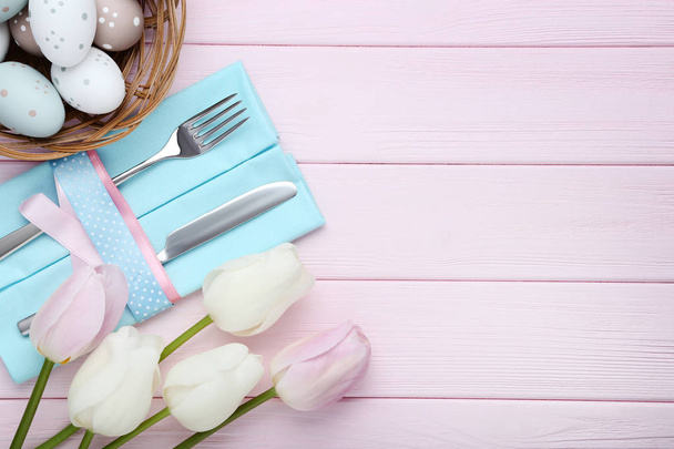 Kitchen cutlery with easter eggs and tulip flowers on pink wooden table - Fotoğraf, Görsel