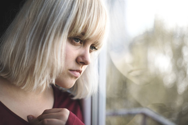 Portrait of sad depressed young woman sitting near window - Zdjęcie, obraz