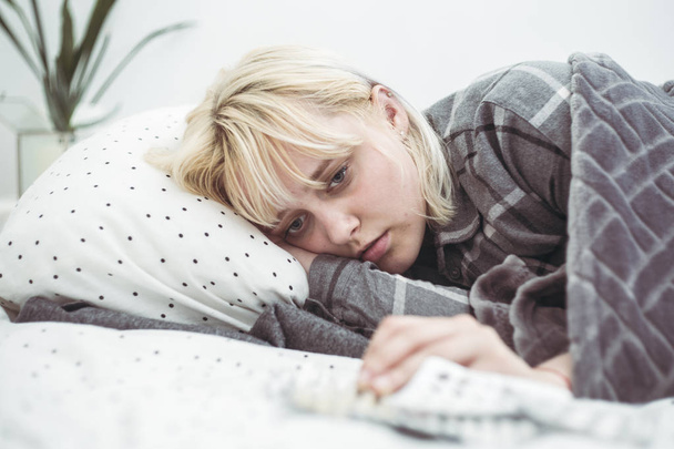 Depressed young woman lying in bed with pile of pills  - Foto, Bild