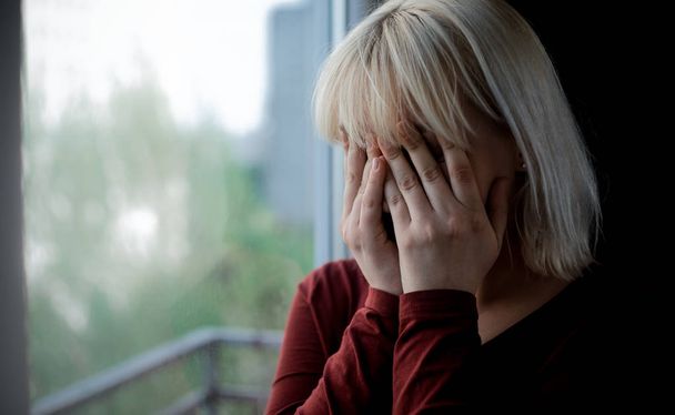 Portrait of sad depressed young woman sitting near window - Фото, изображение