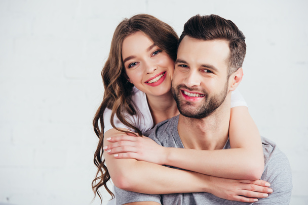 selective focus of happy couple embracing and smiling in white bedroom - Photo, Image