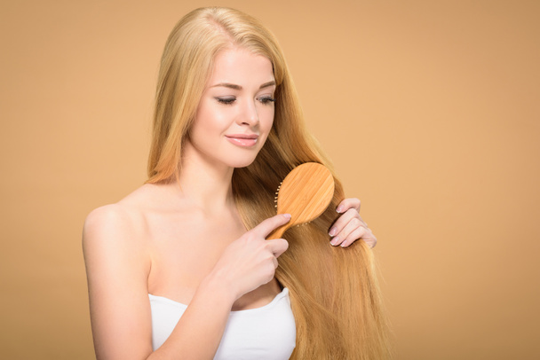 Joyful blonde girl brushing straight hair with smile - Foto, afbeelding