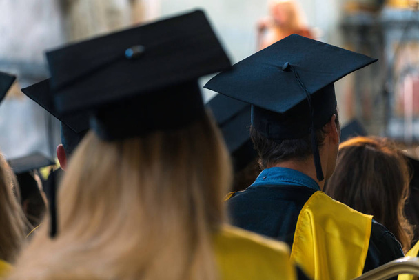 Studenten in Kleidern und Hüten, die drinnen sitzen und auf Diplome warten, Abschlusstag an der Universität, College-Beginn - Foto, Bild