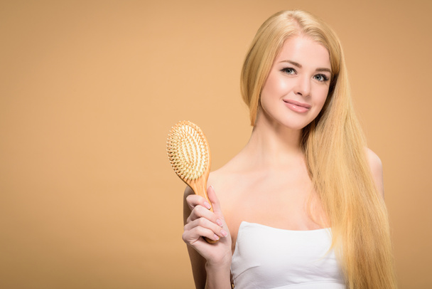 Pretty blonde woman holding wooden hair brush  - Foto, afbeelding