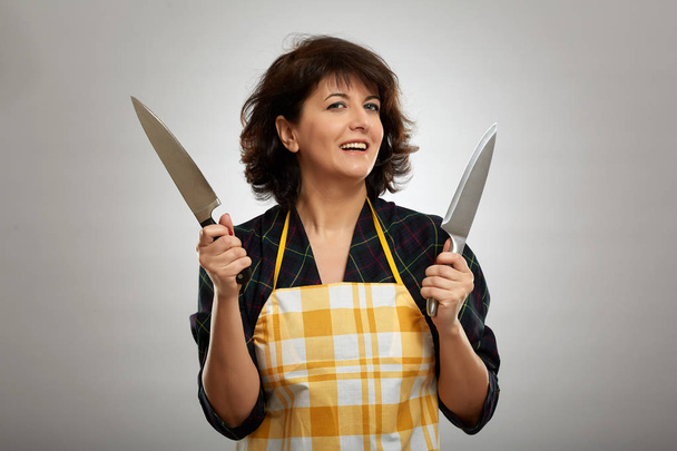 Woman cook holding two chef's knives on gray background - Foto, afbeelding