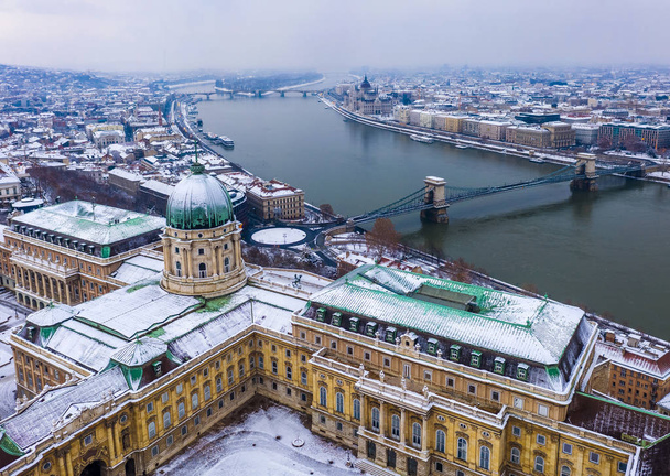Βουδαπέστη, Ουγγαρία - εναέρια θέα στο χιονισμένο Buda Castle βασιλικό παλάτι από πάνω με το Αλυσσιδωτή Γέφυρα των αλυσίδων και το Κοινοβούλιο της Ουγγαρίας στο χειμώνα - Φωτογραφία, εικόνα