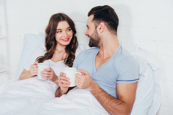 woman and man relaxing, holding cups and looking into eyes - Photo, Image