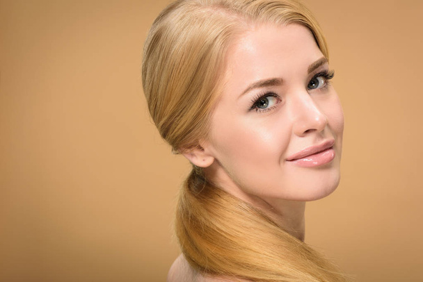 close-up view of attractive blonde girl with long hair smiling at camera isolated on beige - Foto, Imagem
