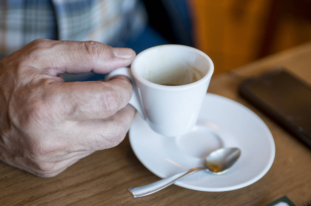 Un hombre tiene en la mano una taza de café expreso en una mesa en un café
 - Foto, Imagen