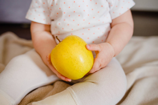 Baby two hands hold yellow apple. Toddler's hands and fresh fruit front view. - Fotografie, Obrázek