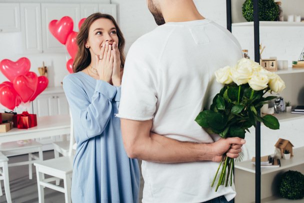 partial view of a young man holding bouquet of roses behind back while smiling girlfriend waiting for surprise - Foto, Bild