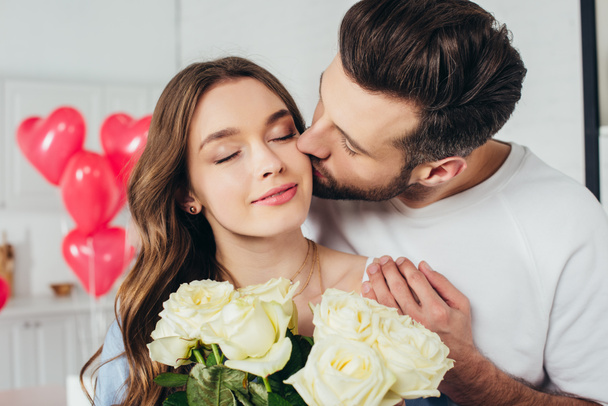 enfoque selectivo de chica feliz sosteniendo rosas ramo con los ojos cerrados mientras novio besar mejilla y abrazar novia
 - Foto, Imagen