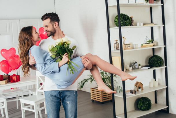 happy couple celebrating st valentine day while young man holding smiling girlfriend with roses bouquet in arms  - Photo, image