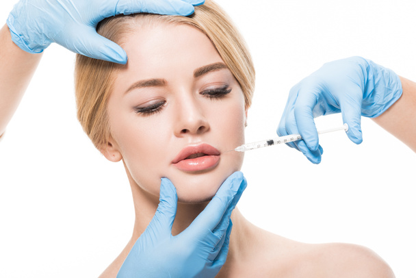 abgeschnittene Aufnahme von Kosmetikerinnen in medizinischen Handschuhen, die einer jungen Frau Schönheitsinjektionen auf weißem Grund verabreichen - Foto, Bild