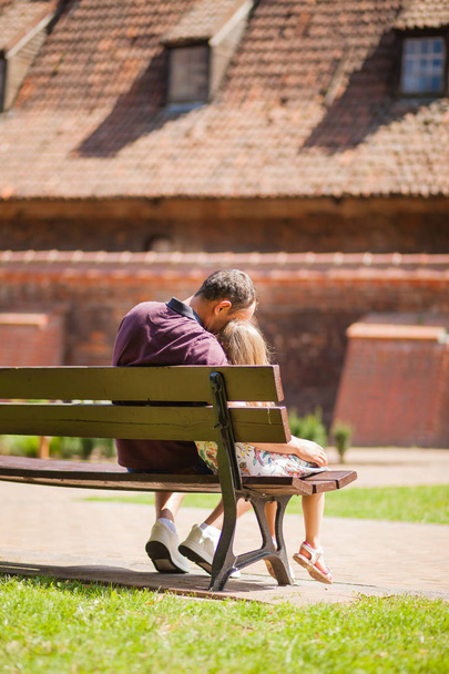 padre e hija se sientan abrazándose en un banco en un parque de la ciudad en verano
 - Foto, imagen