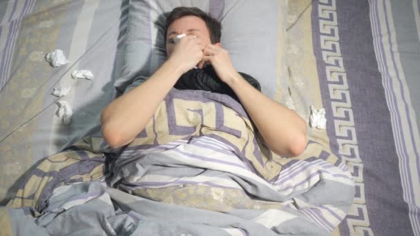 Άρρωστος άνθρωπος με γρίπη και καταρροή σκουπίστε τη μύτη του με ένα χαρτομάντιλο ξαπλωμένοι στον καναπέ στο σπίτι - Πλάνα, βίντεο