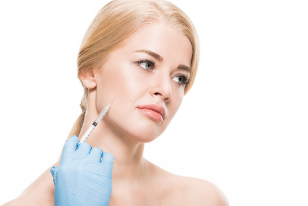 abgeschnittene Aufnahme eines Kosmetikers in Latex-Handschuh, der einer jungen Frau Schönheitsinjektionen auf weißem Grund verabreicht  - Foto, Bild