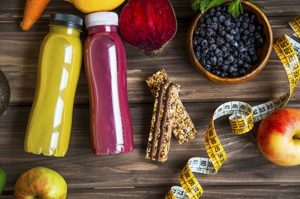 Healthy lifestyle concept with juice bottle, vegetables and fruits with granola muesli bars and measuring tape on wooden board, top view, healthy living fitness concept - Photo, Image