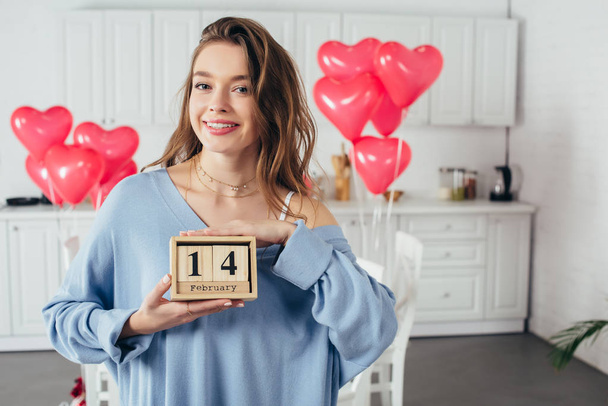 happy smiling girl holding wooden calendar with st valentine day date at home  - Fotografie, Obrázek