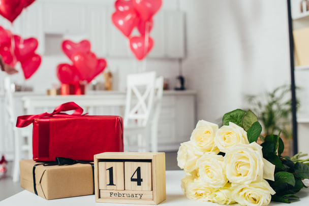 cajas de regalo con cintas, ramo de rosas y calendario con fecha de San Valentín en la mesa con globos en forma de corazón sobre fondo
 - Foto, Imagen