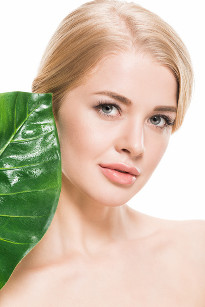attractive naked girl with green tropical leaf near face looking at camera isolated on white - Fotó, kép