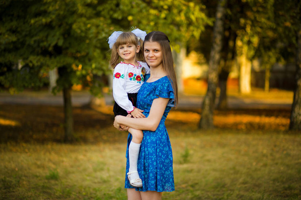 背景秋の公園のお祭り学校制服の美しい若い母親ハグ 1年生の娘の肖像. - 写真・画像