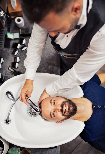 A top view of hipster man client visiting haidresser and hairstylist in barber shop. - 写真・画像