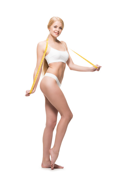 full length view of beautiful young woman in underwear holding measuring tape and smiling at camera isolated on white - Photo, Image