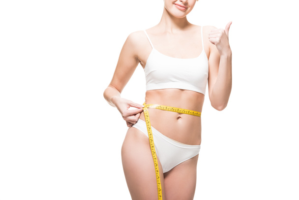 cropped shot of smiling woman measuring waist with tape and showing thumb up isolated on white - Photo, Image