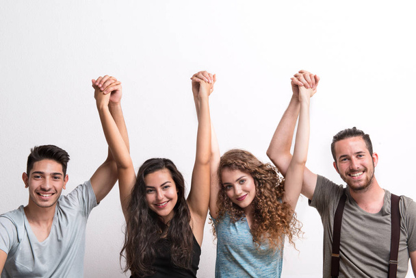 Joyful young group of friends standing in a studio, lifting hands. - Fotografie, Obrázek