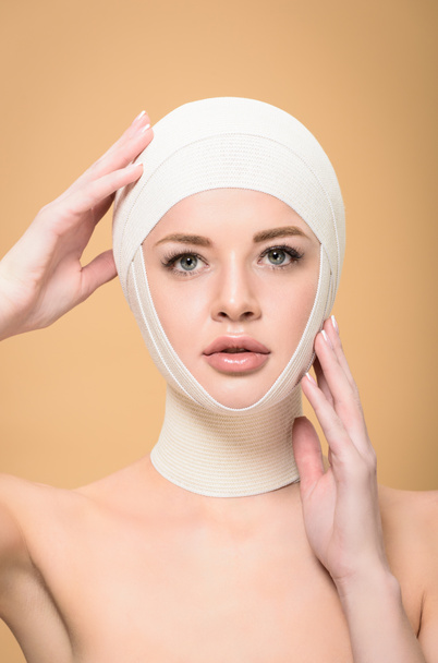 naked young woman touching bandages over head and looking at camera isolated on beige - Foto, Imagem