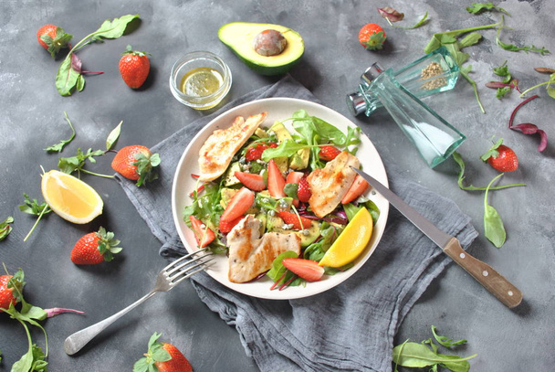 Chicken salad with avocado, strawberries,blue cheese, arugula, beet leaves. Healthy lunch avocado bowl, plate with chicken and strawberries on the dark gray background. Healthy food concept - Φωτογραφία, εικόνα