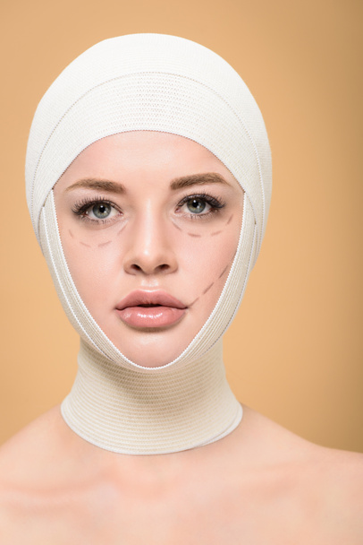 young woman with bandages over head and lines on face looking at camera isolated on beige - Foto, immagini