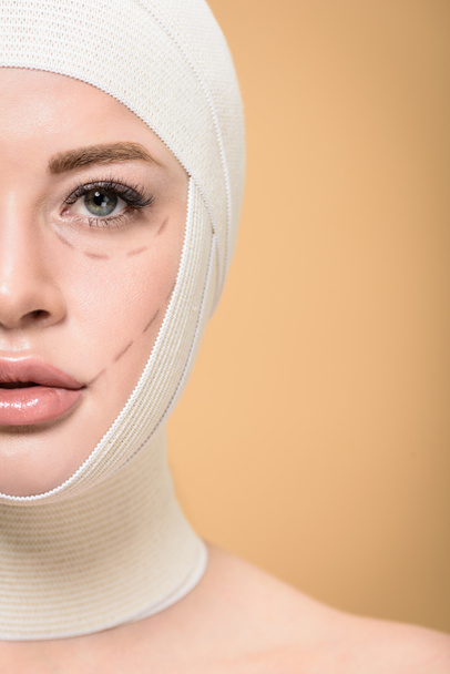 przycięte zdjęcie kobiety z bandaże nad głową i korygowanie znaczników na twarz patrząc na kamery na beżowym tle - Zdjęcie, obraz