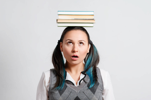 Забавная студентка с пачкой книг на голове. на светлом фоне. концепция образования, студенческая жизнь, эрудиция
 - Фото, изображение