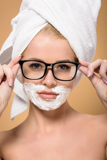 beautiful naked with with towel on head and shaving cream on face adjusting eyeglasses isolated on beige - Foto, Bild