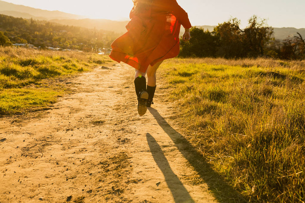 Тан змішана жінка в червоній сукні тікає від глядача до заходу сонця
 - Фото, зображення