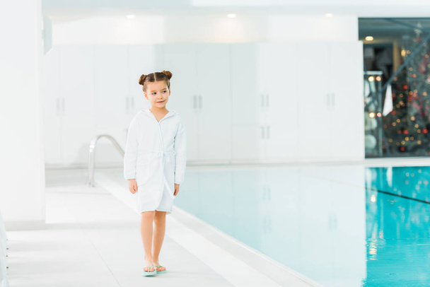 cheerful kid in bathrobe walking near swimming pool  - Foto, Imagem