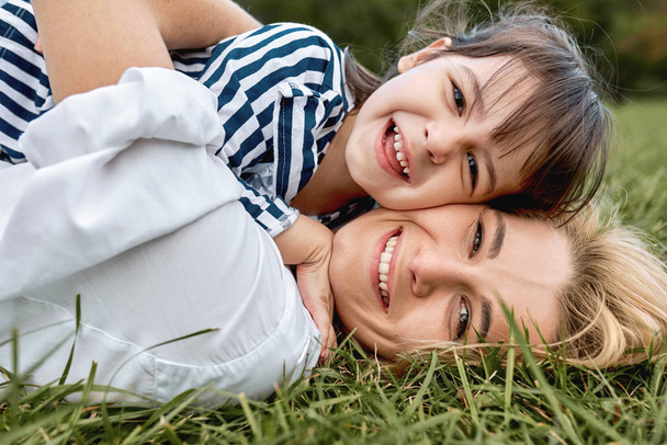 Closeup portrait of pretty woman playing with her cute little girl on green grass outdoor. Loving pretty daughter smiling and embracing her beautiful mother. Happy motherhood, childhood. Mother's day - Фото, зображення