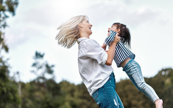 Side view image of happy little daughter playing with her smiling mother in the park. Loving woman and her little kid girl spinning together. Mom and child has fun outdoors. Mother's day - Fotó, kép