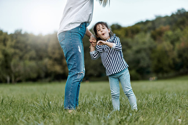 Image of cute happy little girl playing with her beautiful mother outdoors in the park. Happy family time together. Positive emotion. Good relationship between mom and daughter. Mother's day concept - Foto, Imagen