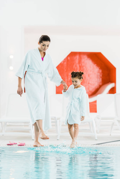 cute kid standing with mother near swimming pool and touching water with legs - Foto, immagini