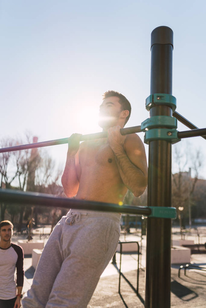 Young athletic guy doing pull up exercises on chin up bar and blue sky in sunny day - Foto, immagini