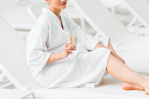 vista cortada da mulher segurando copo de champanhe e sentado em roupão de banho na cadeira deck
  - Foto, Imagem