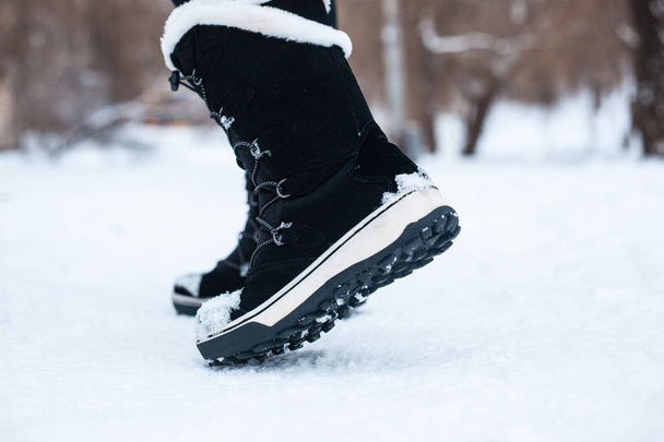 Black winter women's boots with white fur and white soles on the snow in the park - Foto, imagen